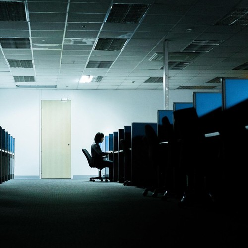 Eine Person sitzt alleine vor einem Computer in einem großen Büro.