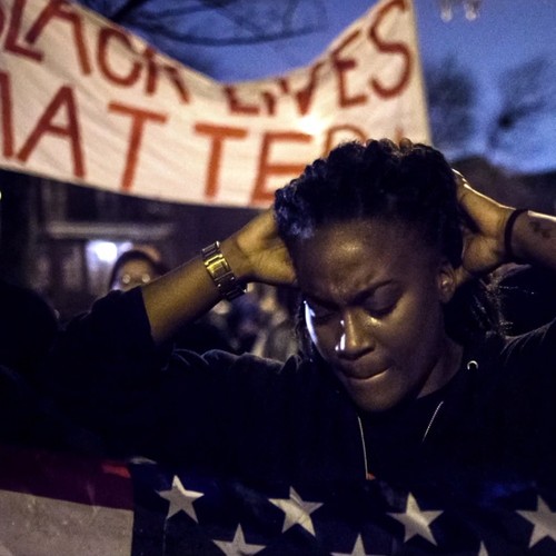 Eine schwarze Frau steht bei einer Demonstration vor einem Banner mit der Aufschrift: Black Lives Matter.