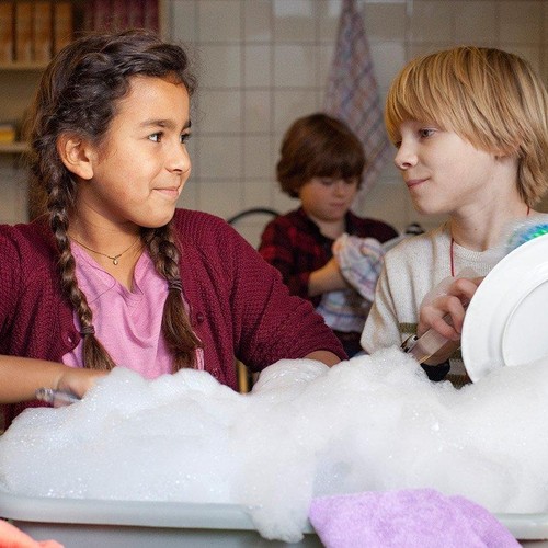 Ein Mädchen und ein Junge spülen Geschirr ab und schauen sich dabei an,