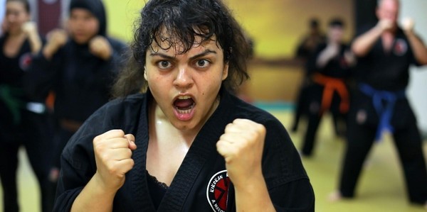 Eine Frau hat im Karatetraining die Hände zu Fäusten geballt und schreit.