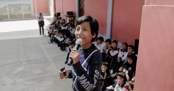 Ein peruanischer Junge spricht vor der Schülerschaft in ein Mikrofon.