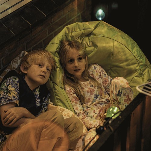 Ein Junge und ein Mädchen liegen in dicken Kissen auf dem Balkon und blicken in den Nachthimmel.