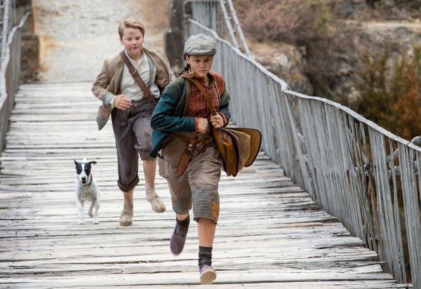 Ein Junge, ein Mädchen und ein Hund rennen über eine Brücke.