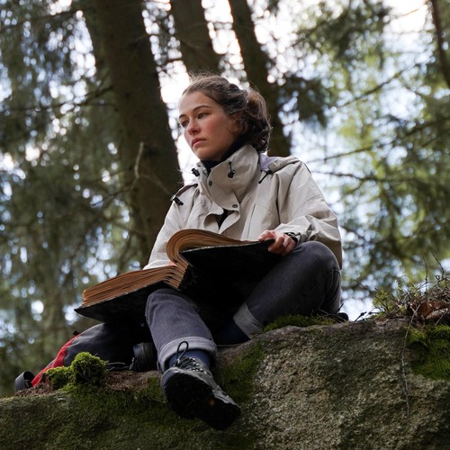 Eine junge Frau sitzt im Wald mit einem Buch auf dem Schoß.