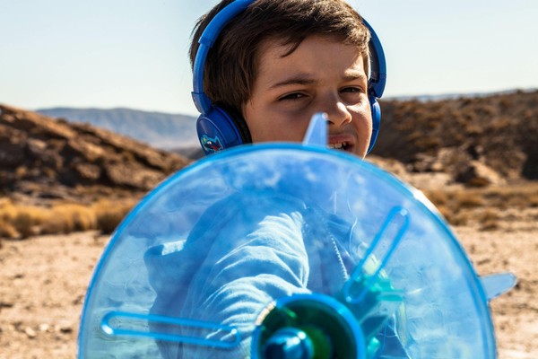 Ein Junge trägt blaue Kopfhörer und hält einen ebenso blauen Empfänger in der Hand.