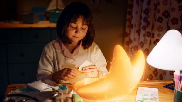 Ein kleines Mädchen sitzt am Schreibtisch und klebt ein Pflaster auf einen leuchtenden Stern.