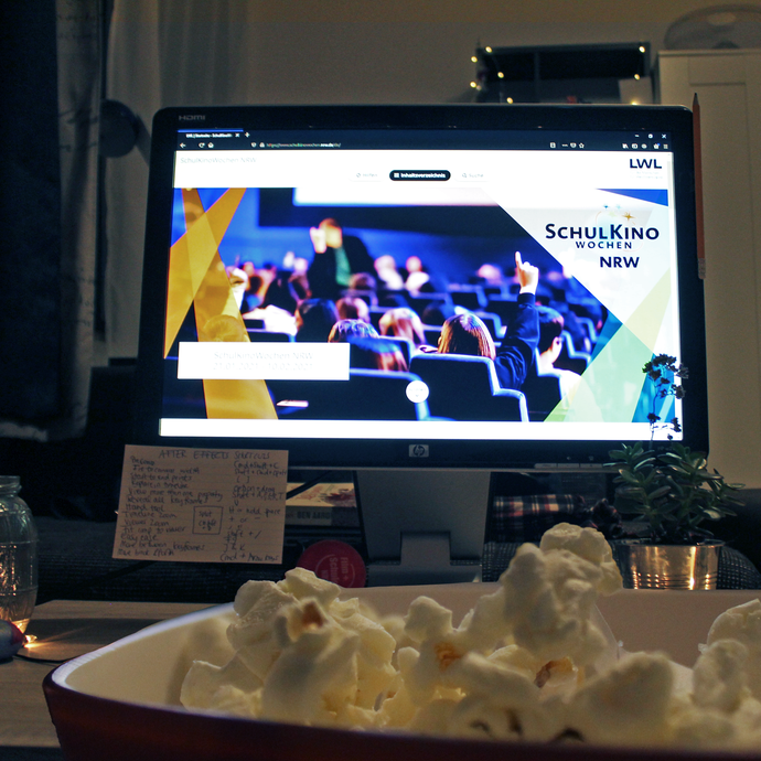 Ein Tisch mit einem Fernseher, auf dem man die Startseite der SchulKinoWochen Webseite sieht. Im Vordergrund steht eine Schüssel Popcorn. (vergrößerte Bildansicht wird geöffnet)