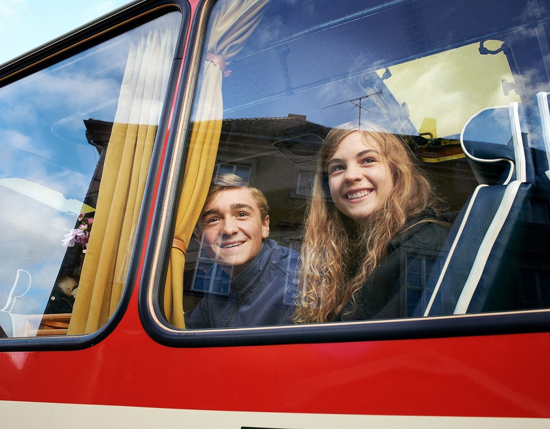 Ein Junge und ein Mädchen blicken aus einem Busfenster nach draußen.