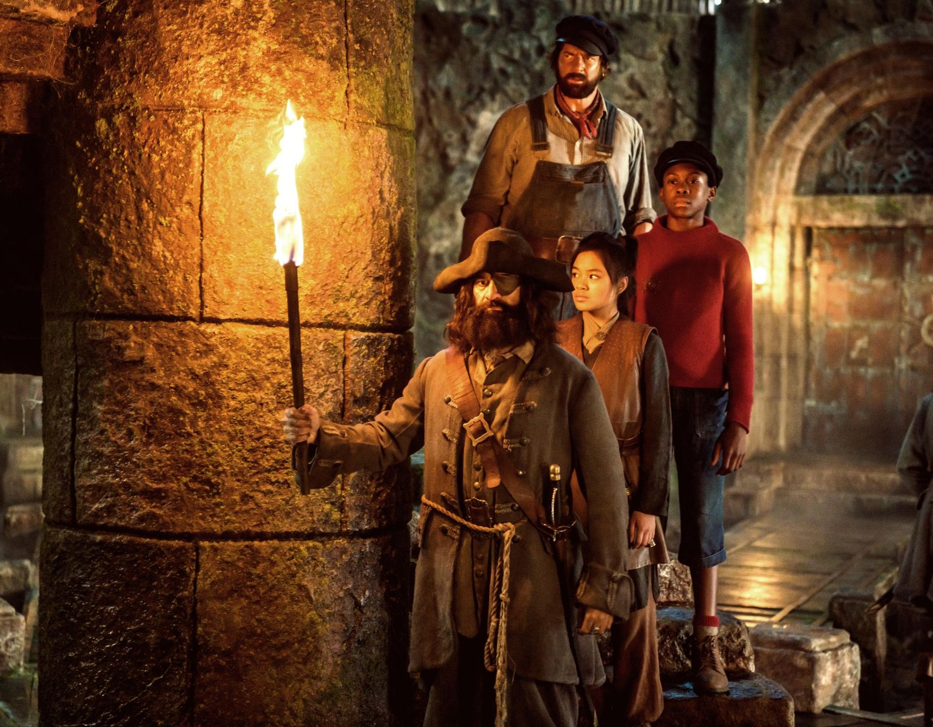 Ein Pirat steht mit einer Fackel in der Hand in einem Gewölbe, hinter ihm Prinzessin Li Si, Jim Knopf und Lukas, der Lokomotivführer.