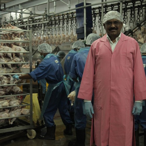Ein Mann blickt in die Kamera. Hinter ihm wird Hühnerfleisch produziert.