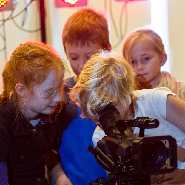 Eine Gruppe Schülerinnen und Schüler umringt eine Kamera und schaut durch den Sucher.